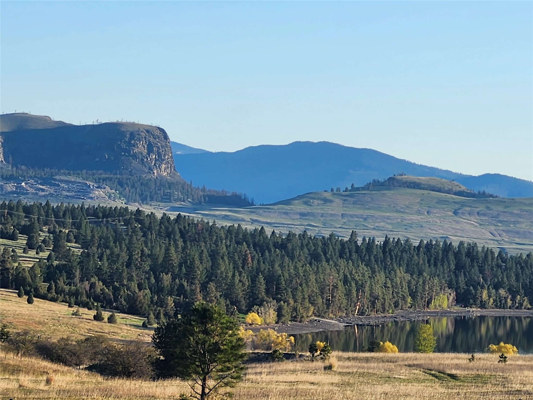 Mountain lake beyond a pine forest, with a rocky bluff and golden autumn trees.
