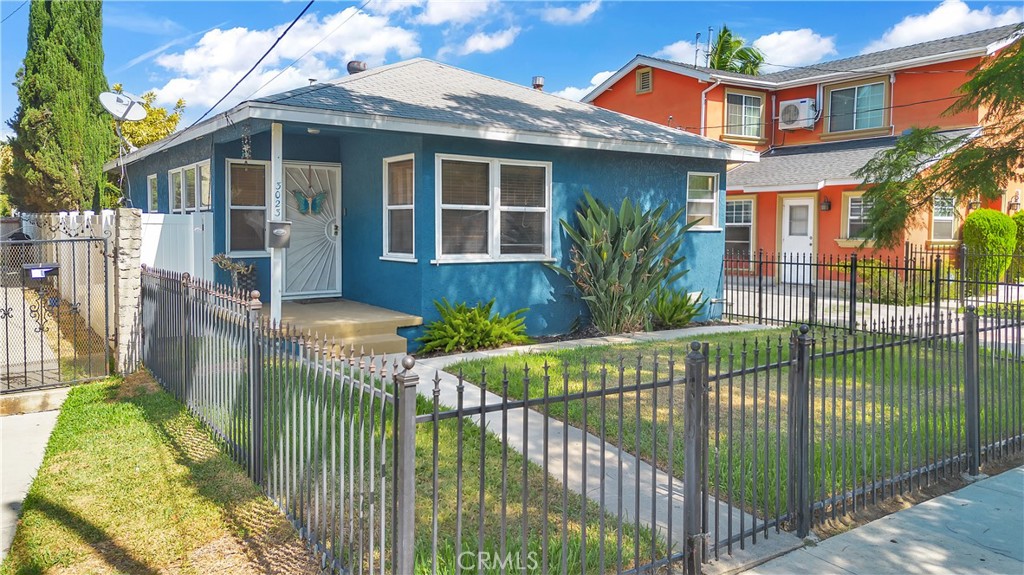 Blue single-story home behind a black metal fence, with an orange neighboring house.