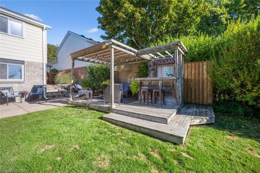 Backyard deck with a wooden pergola, outdoor bar, and seating beside a green lawn.