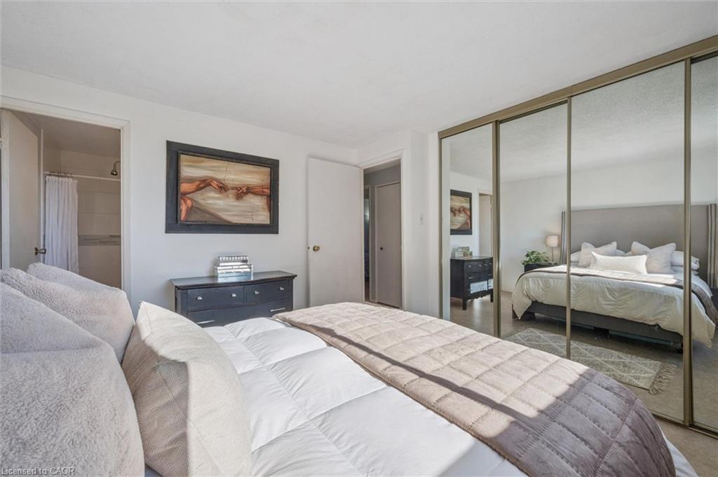 Bedroom with a large white bed, mirrored closet doors, and dark dresser.