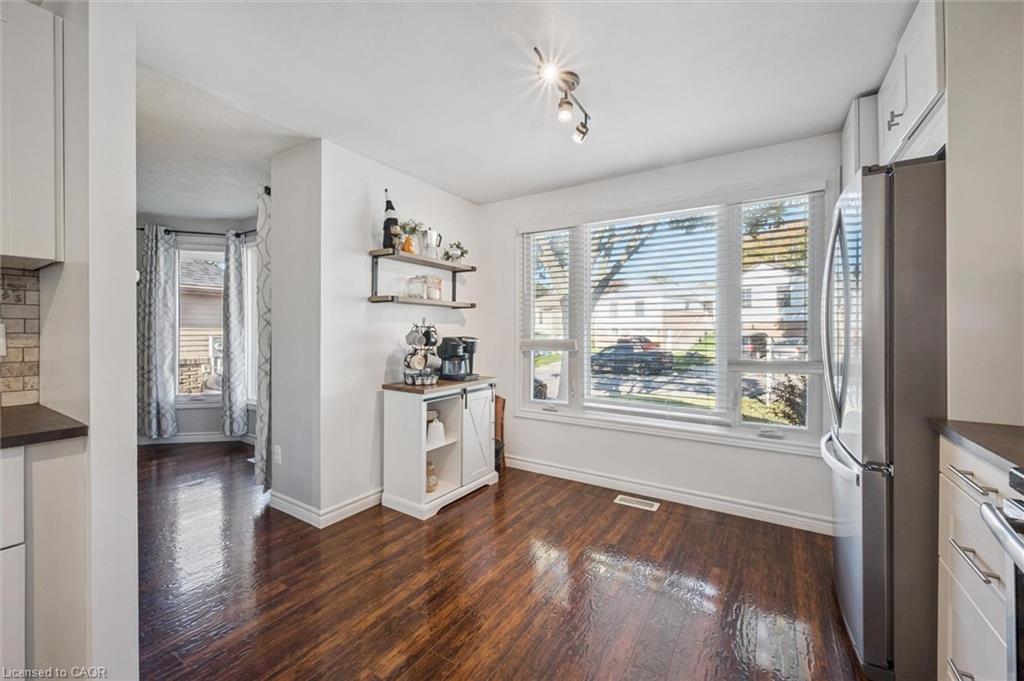 Bright kitchen and dining area with dark hardwood floors, large window, and stainless steel refrigerator.