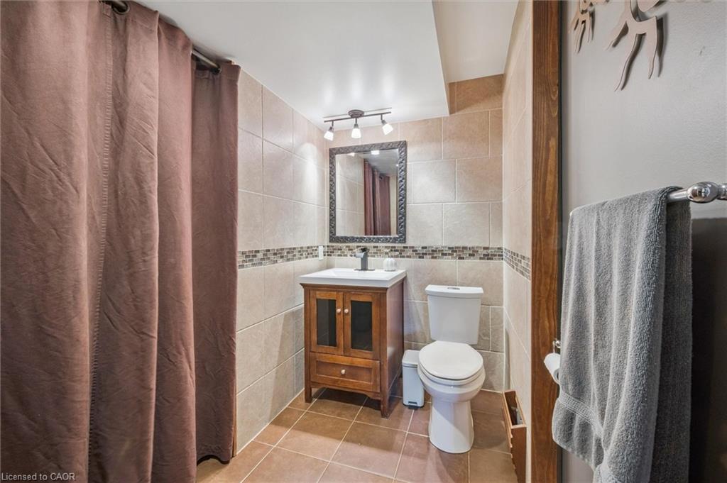 Tiled bathroom with a wooden vanity, white toilet, and brown shower curtain.