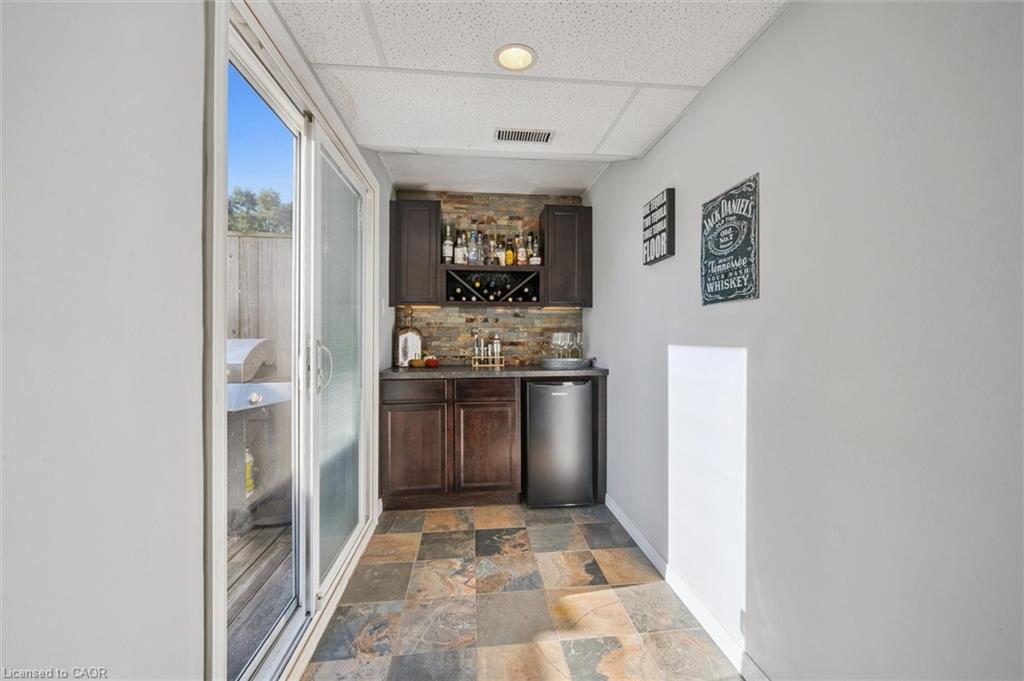 Home bar with dark wood cabinets, bottle display, stone backsplash, and sliding glass doors.