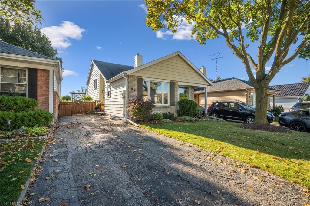 Single-story house with a paved driveway, front lawn, and large shade tree.