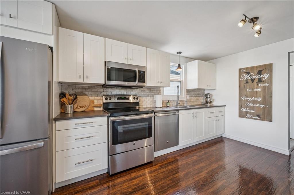 Kitchen with white cabinetry, stainless steel appliances, tiled backsplash, and dark hardwood floors.