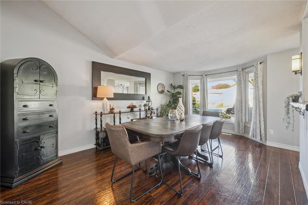 Dining room with a dark wood table, upholstered chairs, polished floors, and a large curtained window.