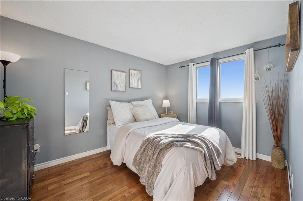 Staged bedroom with a white bed, gray walls, hardwood floors, and two curtained windows.