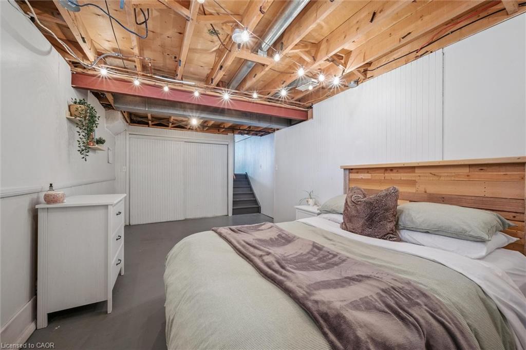 Basement bedroom with a wooden bed frame, exposed ceiling joists, and stairs at the back.