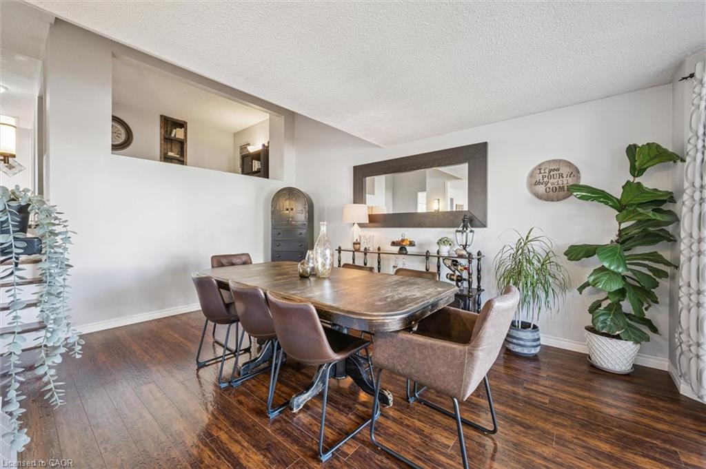 Dining room with a large wooden table, upholstered chairs, dark hardwood floors, and leafy plants.