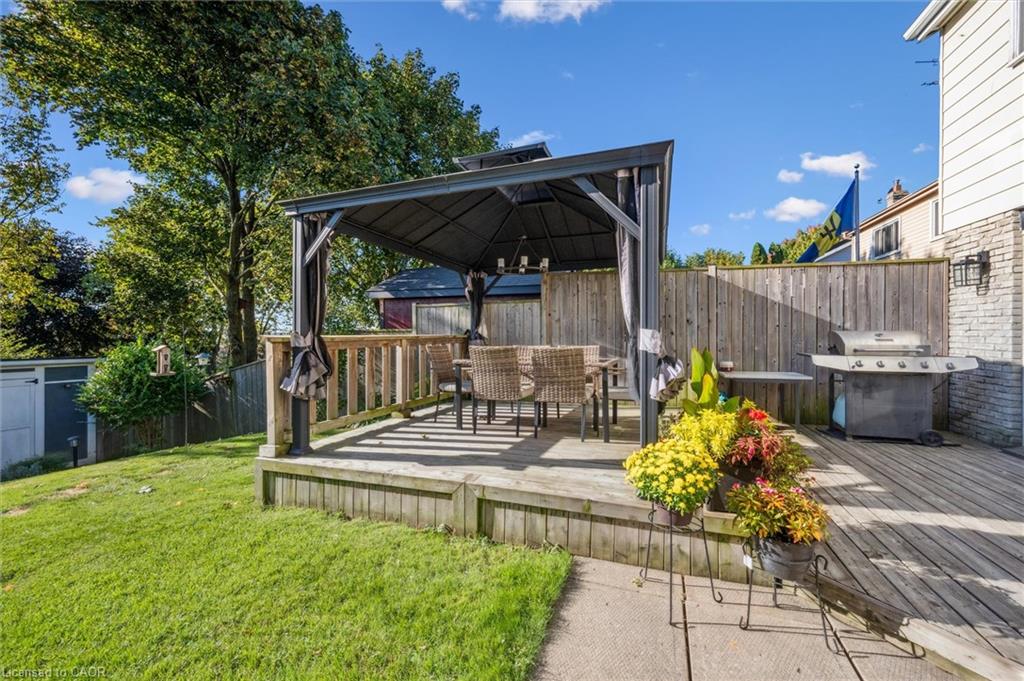 Backyard deck with a covered gazebo, dining set, barbecue grill, and fenced lawn.