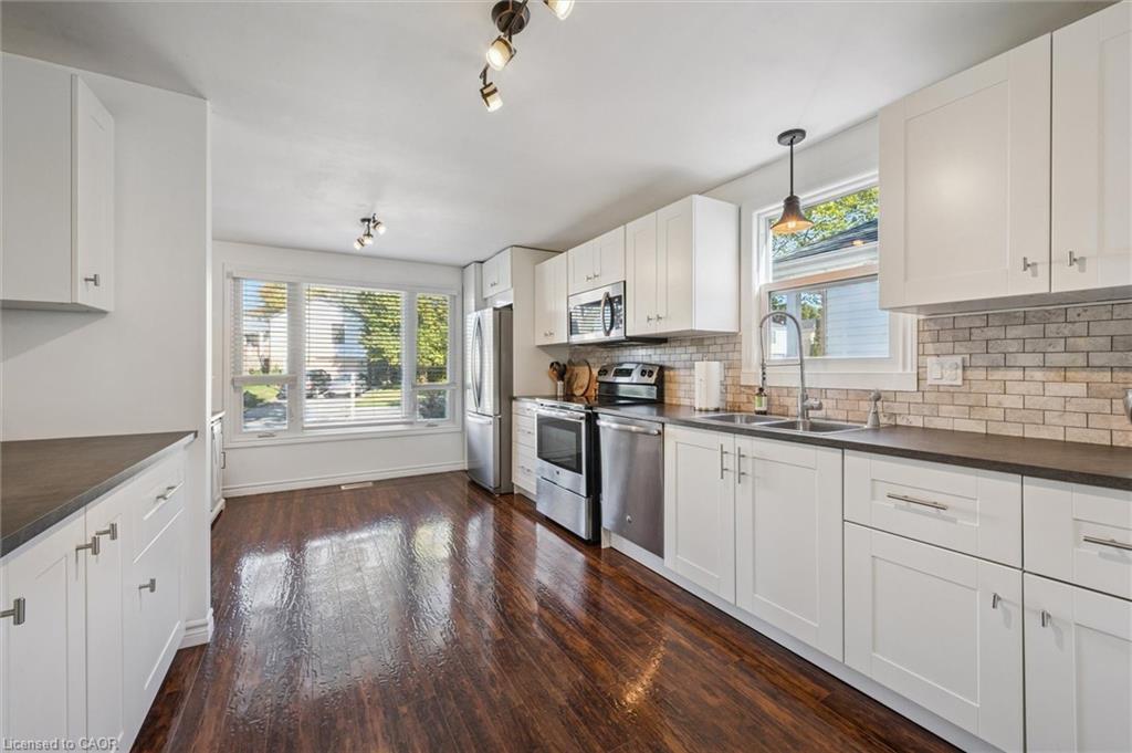 Kitchen with white cabinets, stainless steel appliances, brick-tile backsplash, and dark wood floors.