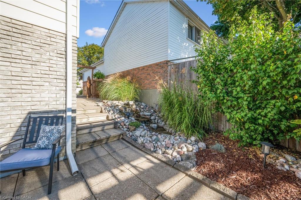 Side patio with paved walkway, steps, river-rock garden, and a cushioned chair beside the house.