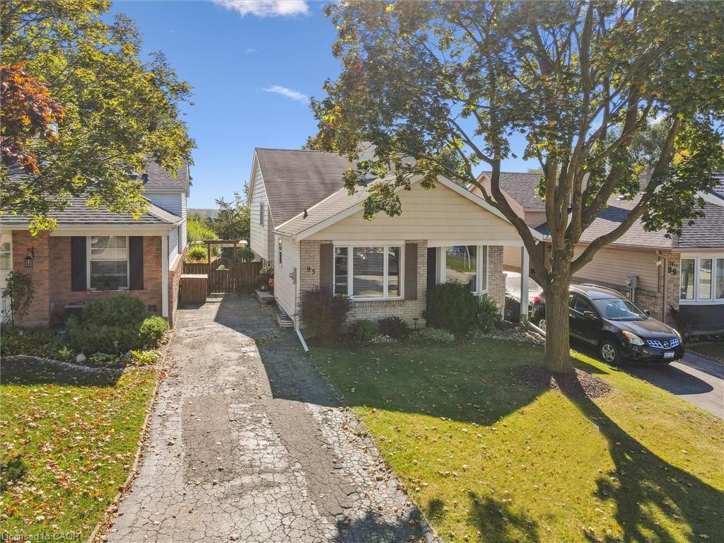 Single-story house with a front gable, brick accents, paved driveway, and mature autumn trees.