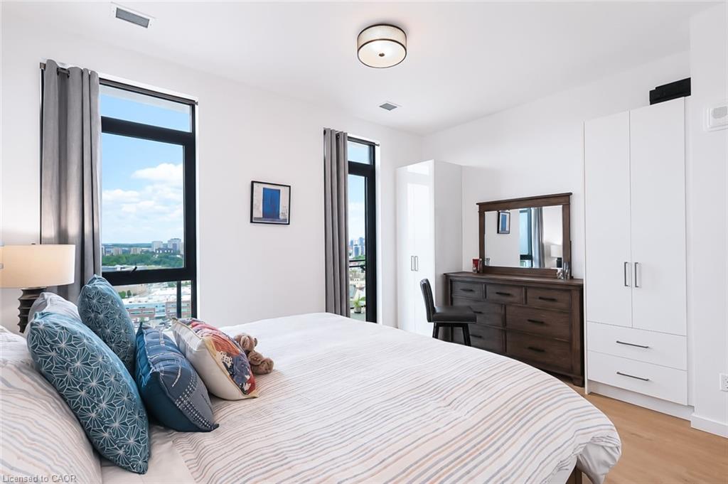 Furnished condo bedroom with a large bed, city views through tall windows, and white built-in wardrobes.