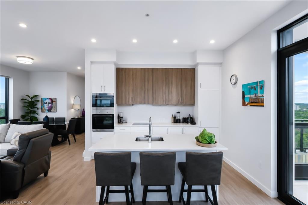 Open-plan condo kitchen with a white island, dark bar stools, and large windows overlooking greenery.