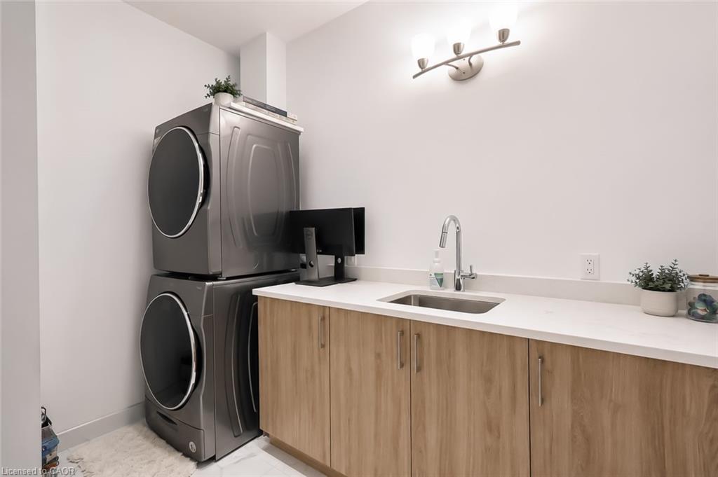 Laundry room with stacked washer and dryer, light wood cabinets, and a countertop utility sink.