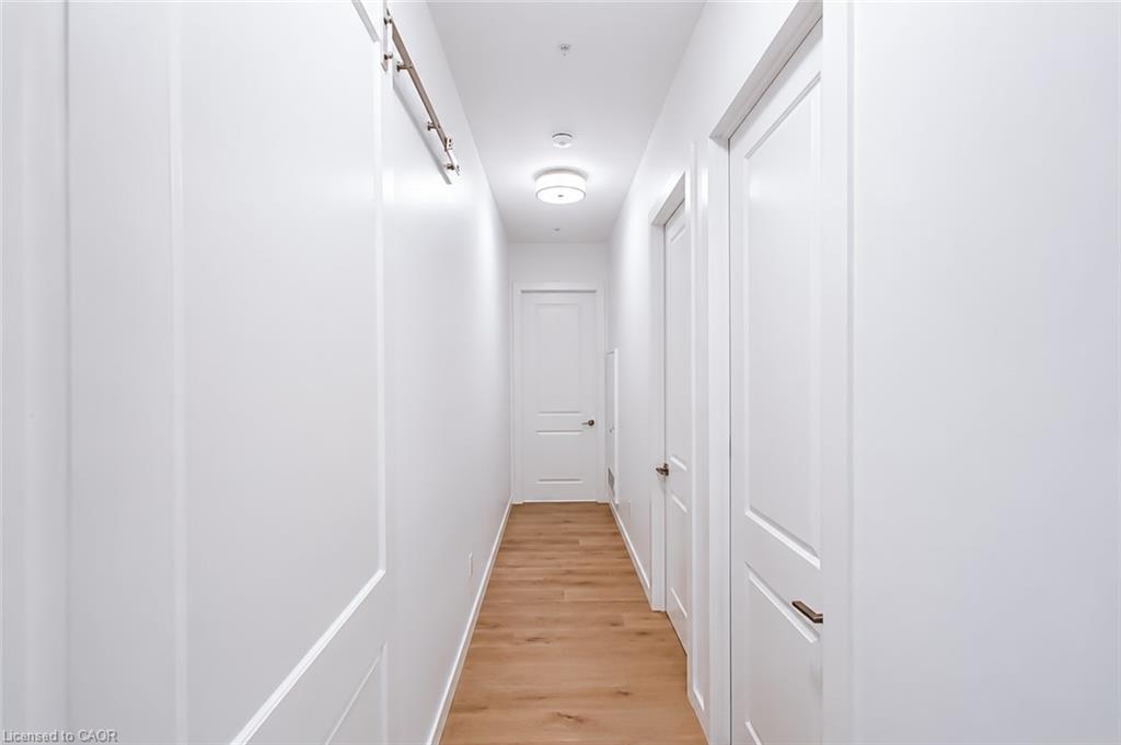 Apartment hallway with white paneled walls, multiple doors, and light wood flooring.