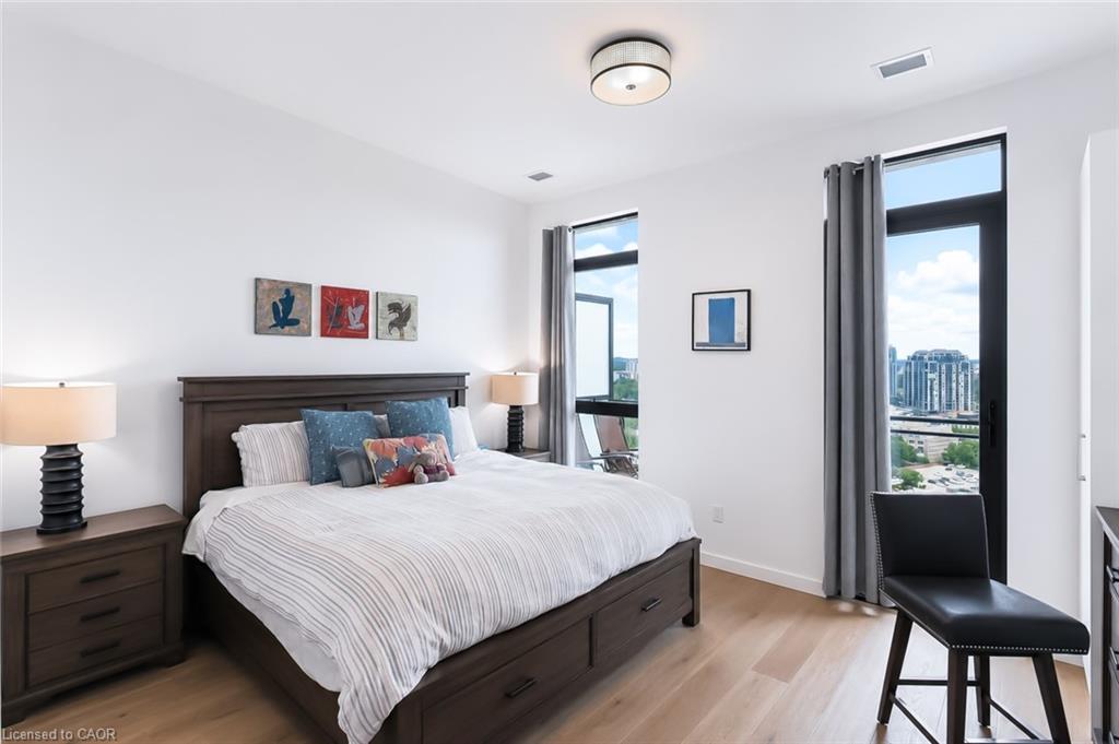 Furnished bedroom with a dark wood bed and tall windows overlooking city buildings.