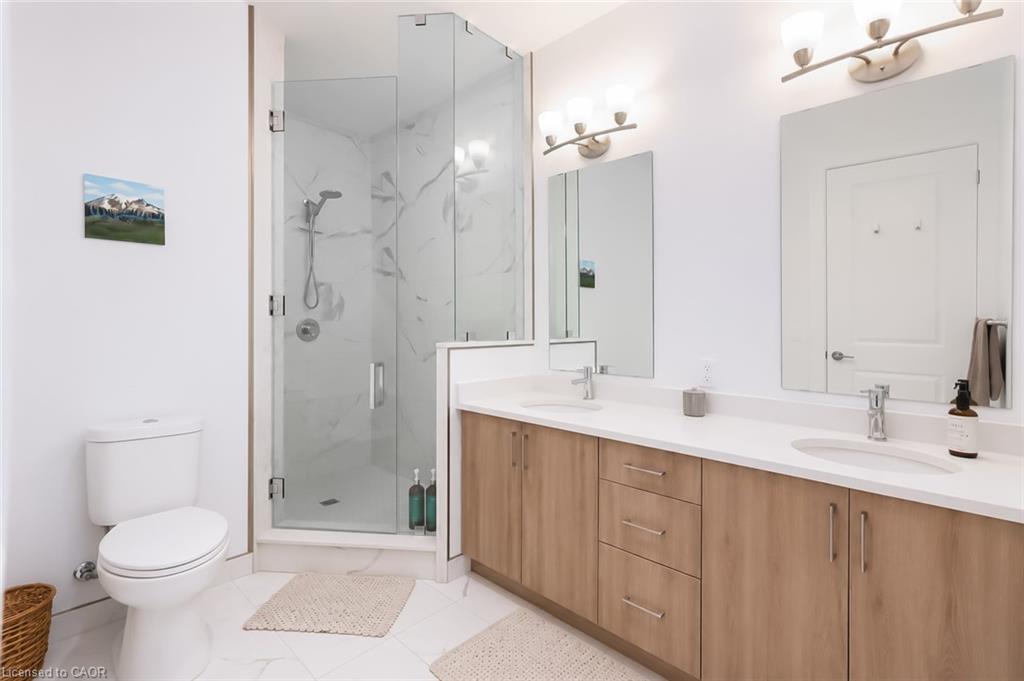 Modern bathroom with a glass shower, double-sink wood vanity, and white tile floors.