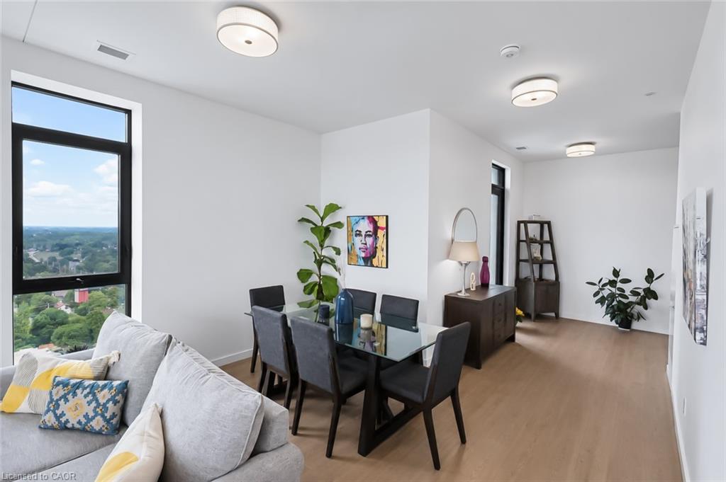 Condo living and dining area with a glass table and large windows overlooking a green urban landscape.