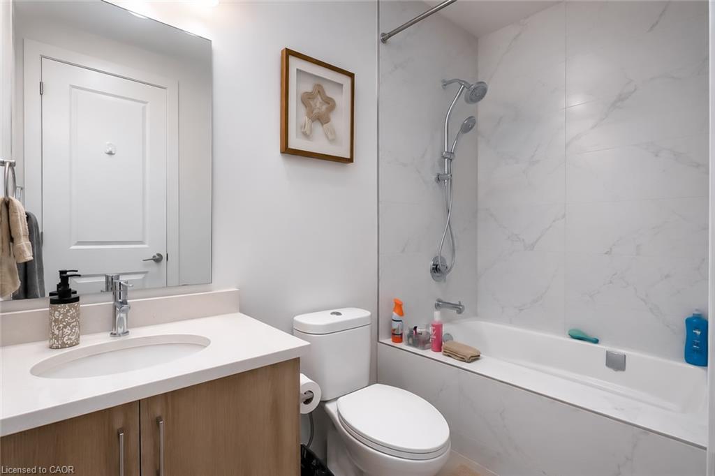 Modern bathroom with a white vanity, wood cabinetry, and a marble-look tub surround.