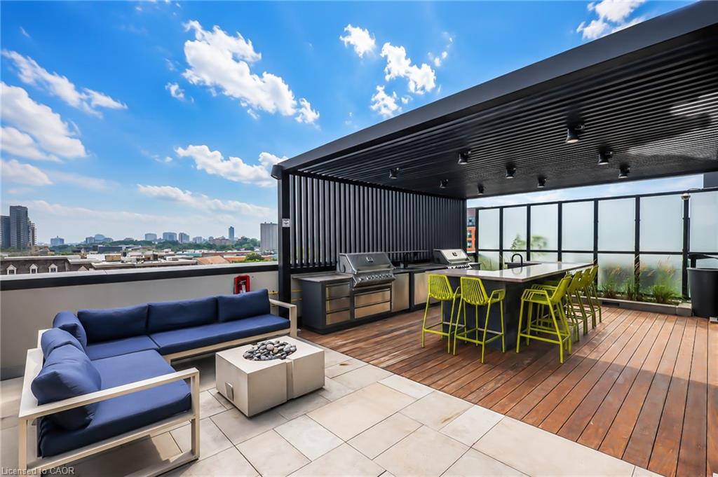Rooftop terrace with lounge seating, yellow dining chairs, two grills, and city skyline views.