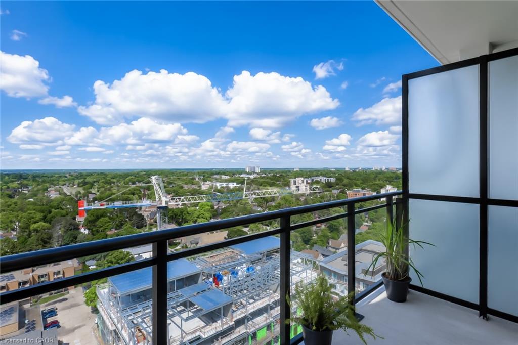 High-rise condo balcony overlooking leafy Waterloo neighborhoods and a construction site, with glass railings and potted plants.