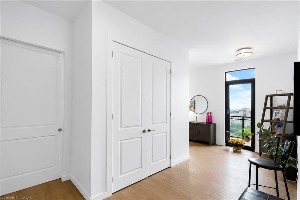 Condo entry hall with white paneled doors, light wood floors, and a balcony door overlooking the city.