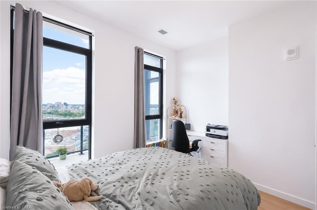 Bedroom with a bed, tall curtained windows, and a desk overlooking city buildings.