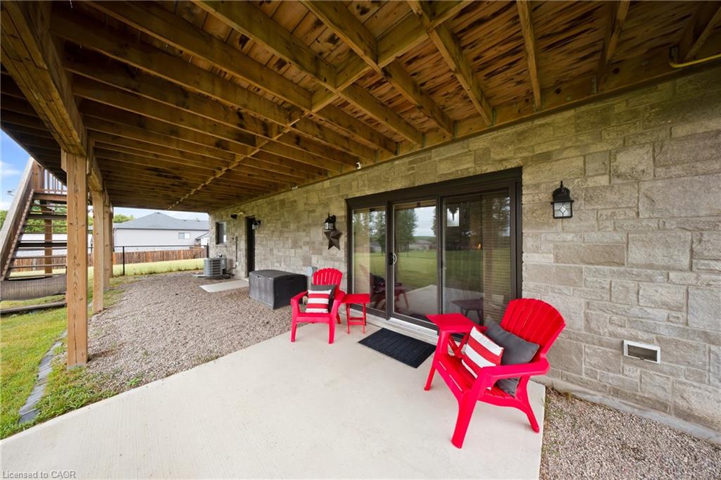 Covered patio with red Adirondack chairs beneath a wood-framed deck beside a stone wall.