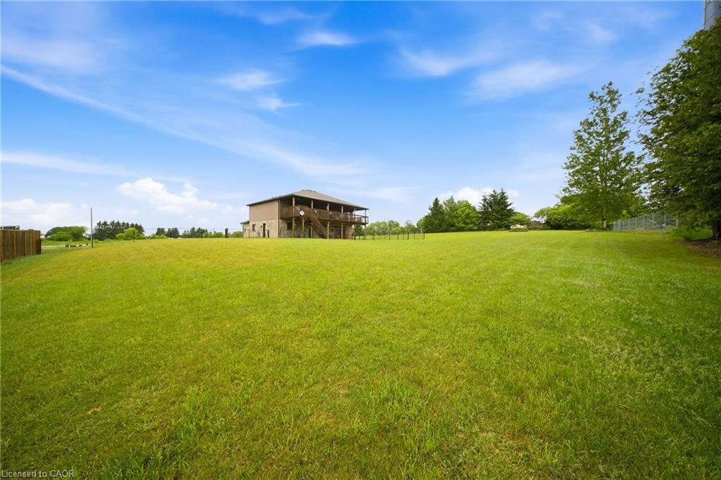 Two-story home with a raised deck beyond a broad green lawn and mature trees.