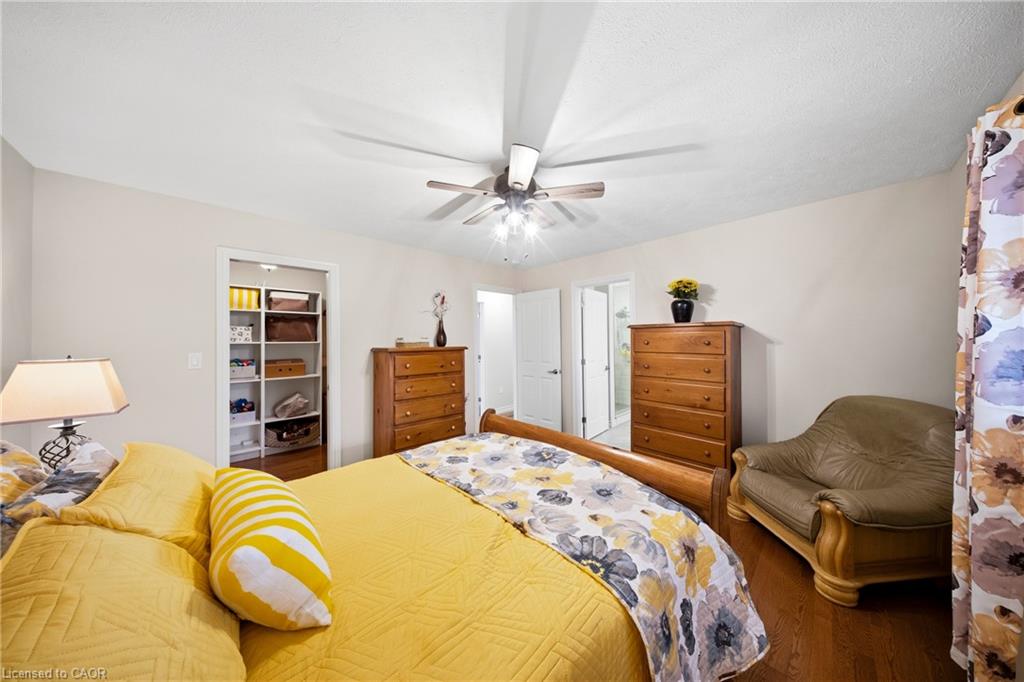Bedroom with a yellow bed, floral bedding, ceiling fan, wooden dressers, and leather armchair.