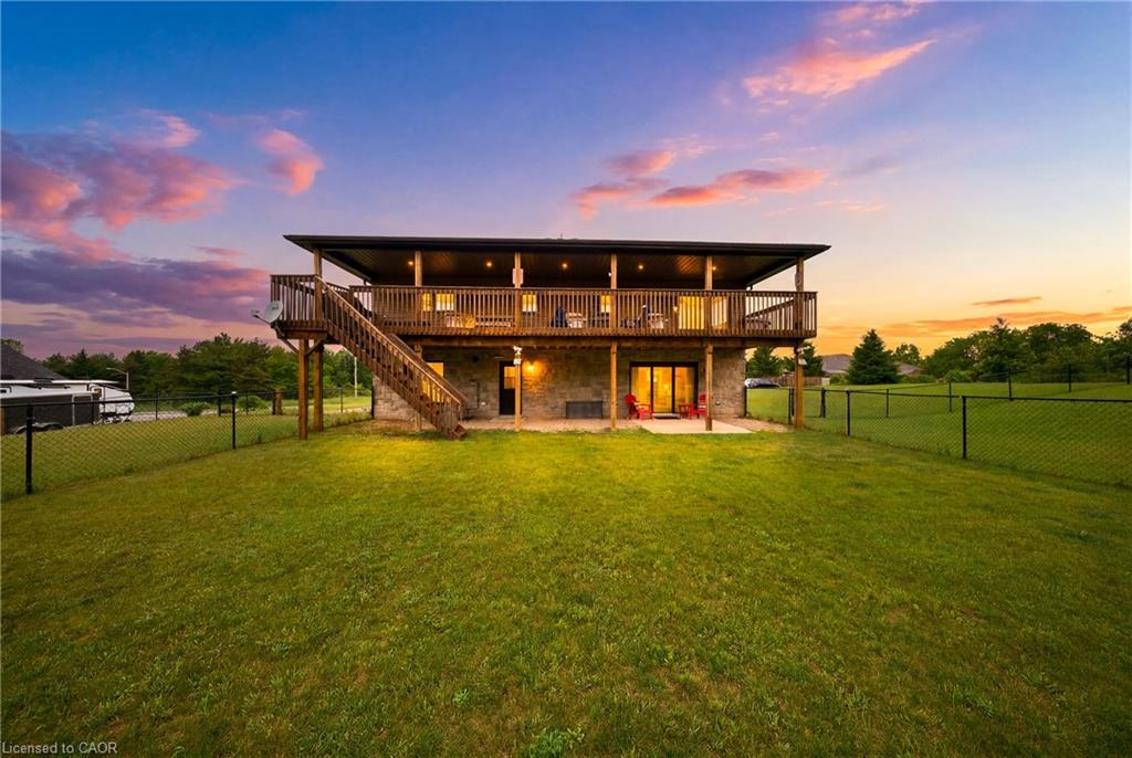 Two-story stone-and-wood home with a raised deck and fenced lawn at sunset.