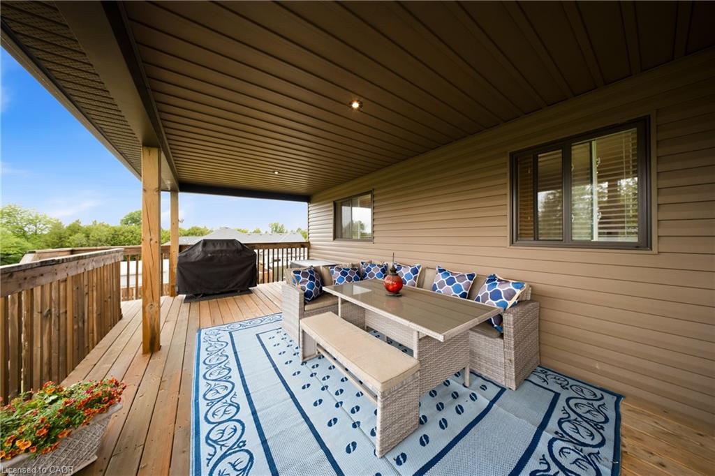 Covered wooden deck with wicker seating, a blue-and-white rug, and a covered grill.