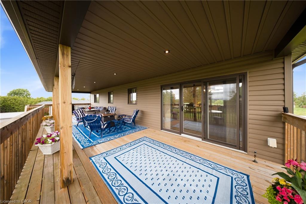 Covered wooden deck with blue patio seating, patterned rugs, sliding glass doors, and flower planters.