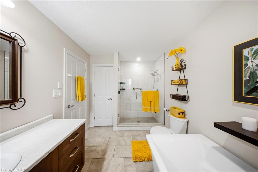 Bathroom with a glass-enclosed shower, white tub, wood vanity, and bright yellow towels.