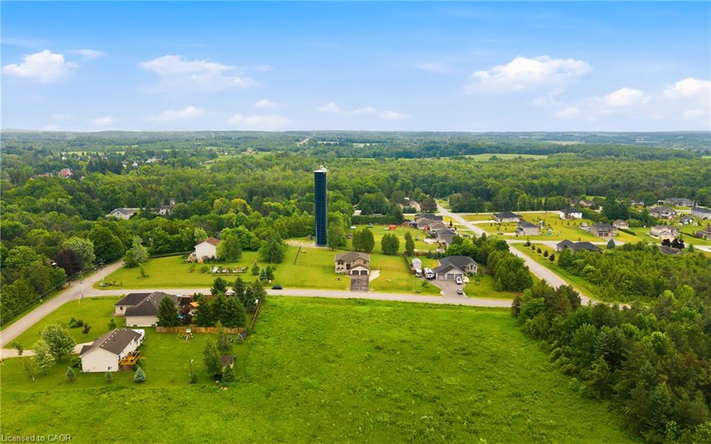 Aerial view of a grassy property lot amid rural homes and wooded countryside.