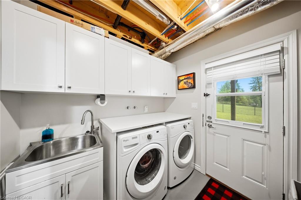 Laundry room with white cabinets, stainless utility sink, front-loading washer and dryer, and a glass-panel door.
