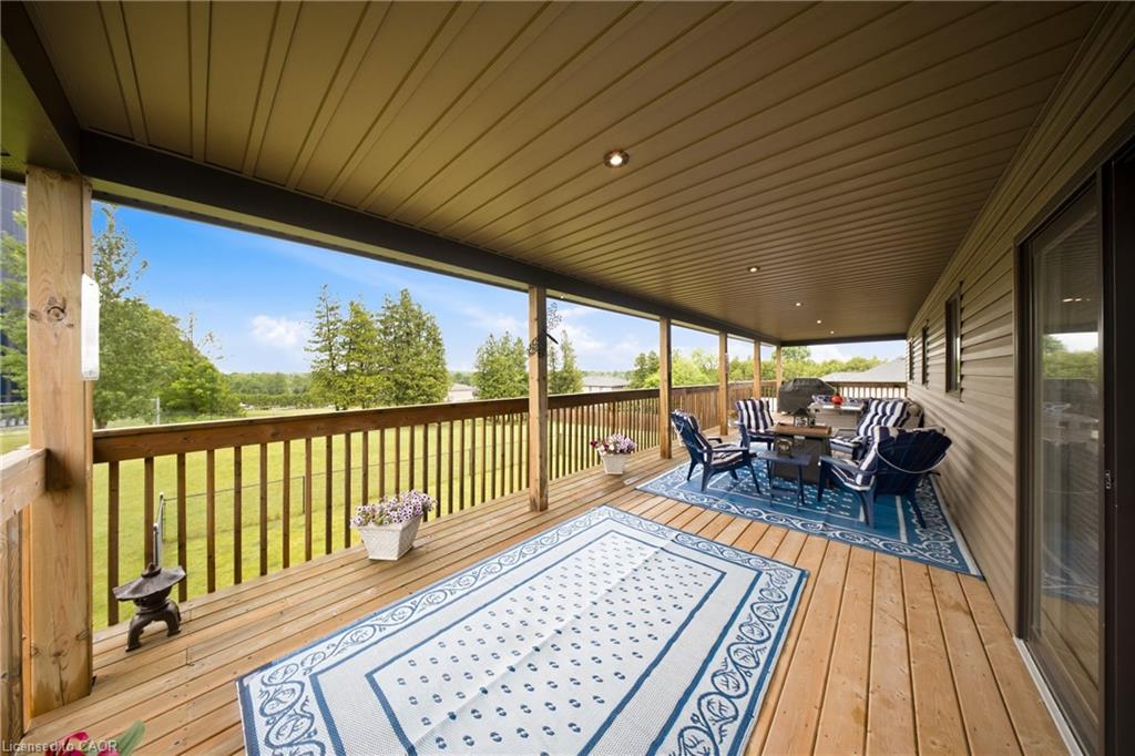Covered wooden deck with blue-and-white rugs, outdoor seating, and views over a green lawn and trees.