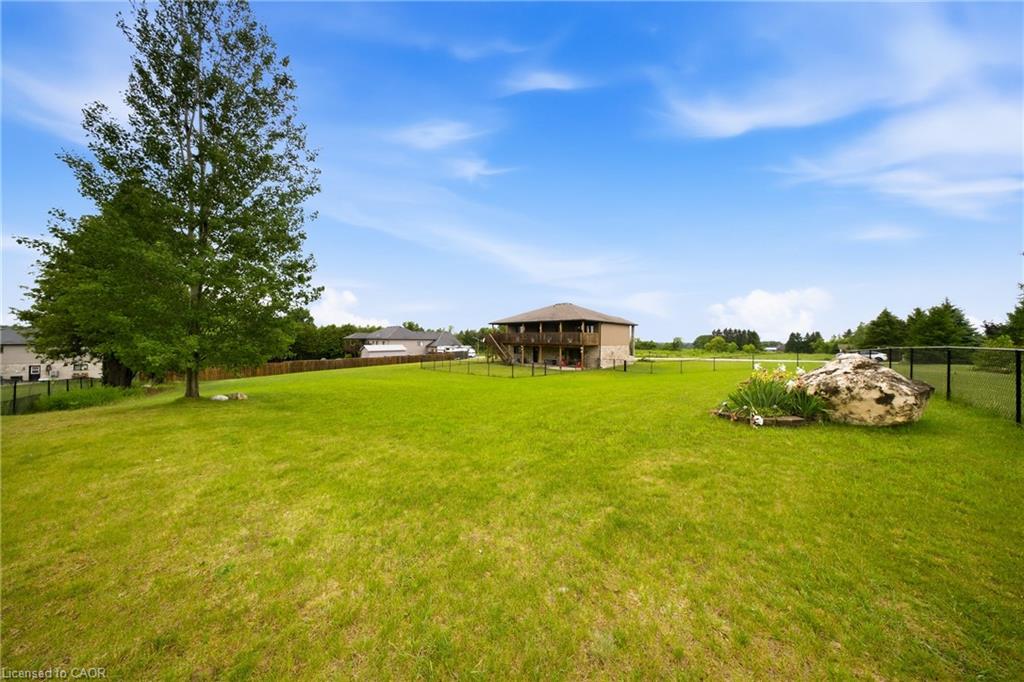 Fenced lawn behind a two-story home, with a raised deck, mature tree, and landscaped boulder.