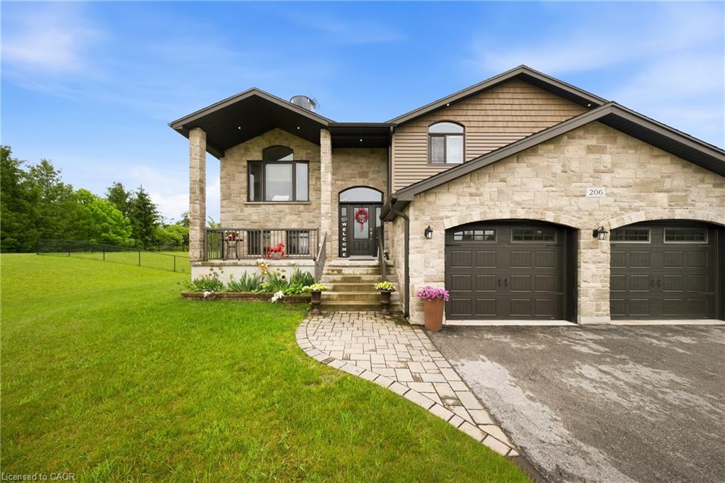 Two-story stone house with a covered porch, double garage, and curved paver walkway across a broad lawn.