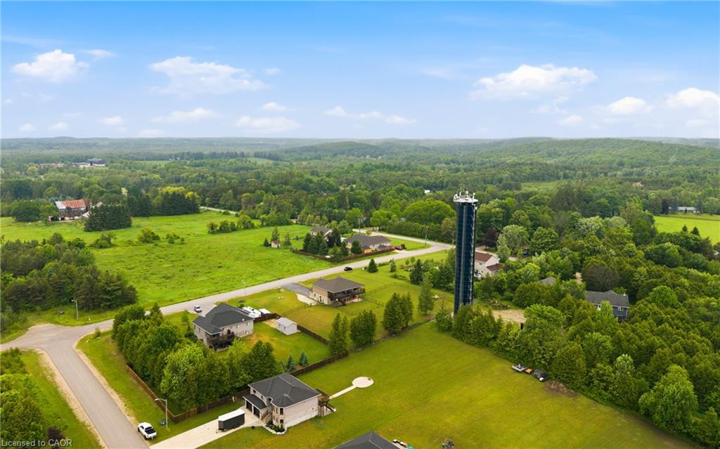Aerial view of spacious homes and green lots beside wooded countryside and rolling hills.