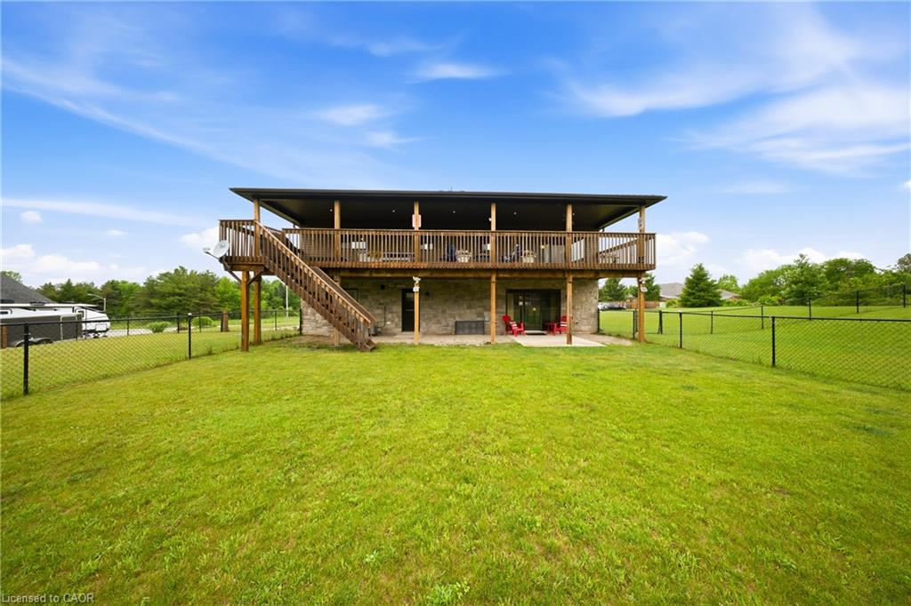 Rear of a two-story home with a covered wooden deck, exterior stairs, and a large fenced lawn.