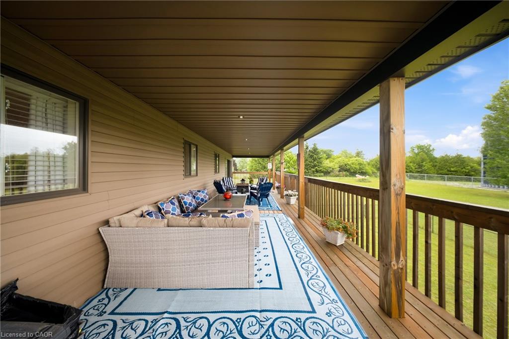 Covered wooden deck with wicker seating and blue patterned rugs overlooking a green lawn.