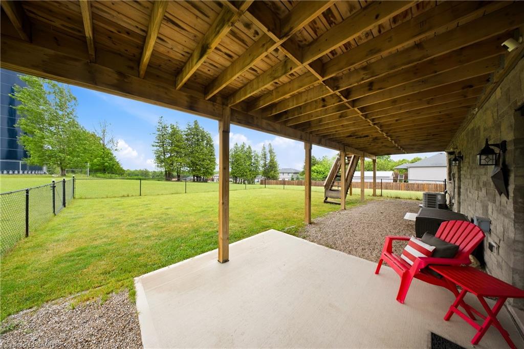 Covered backyard patio with exposed timber beams and red Adirondack chairs overlooking a fenced lawn.