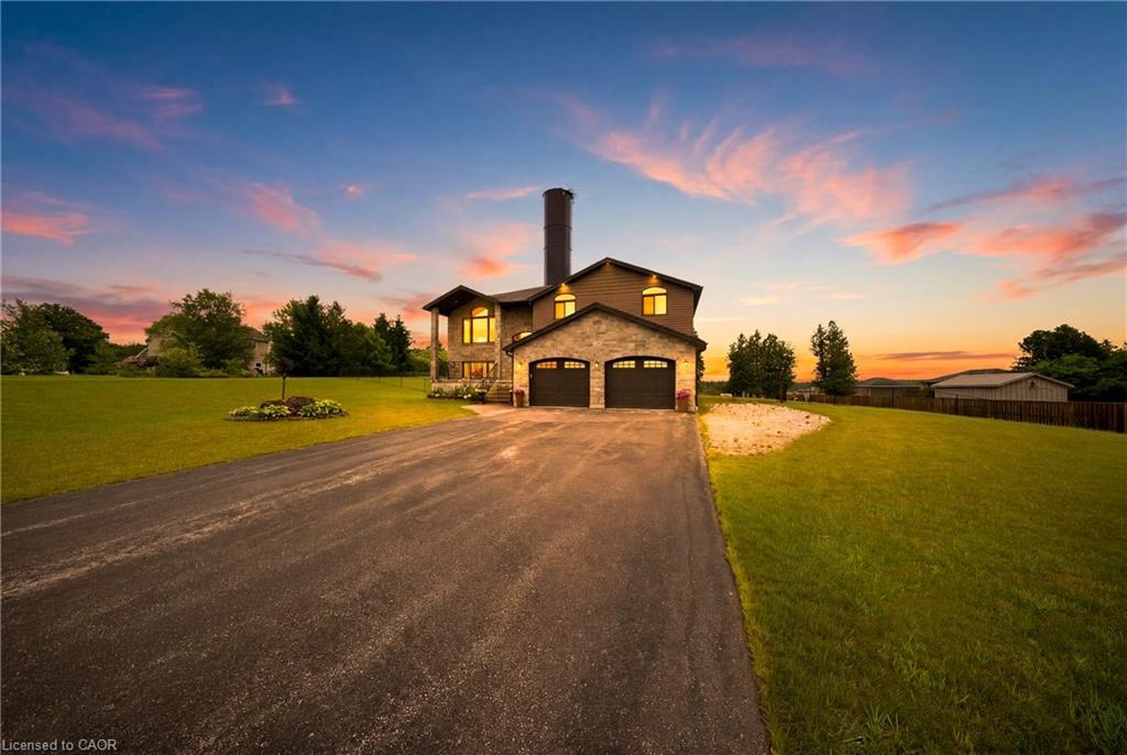 Two-story stone-fronted home with a double garage, long driveway, and sunset sky.