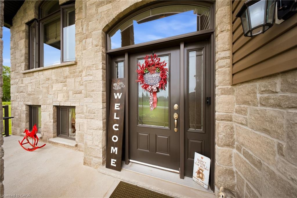 Stone home entry with a dark brown door, welcome wreath, vertical welcome sign, and red rocking horse.