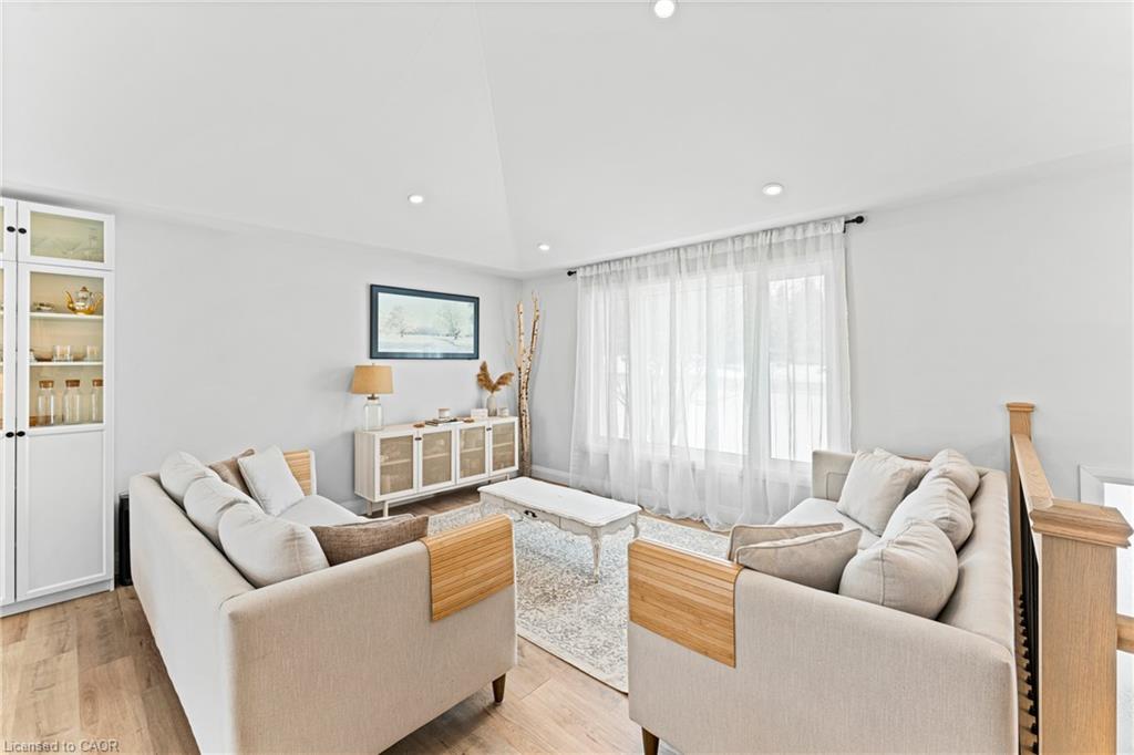 Furnished living room with cream sofas, a patterned rug, and large windows with sheer curtains.