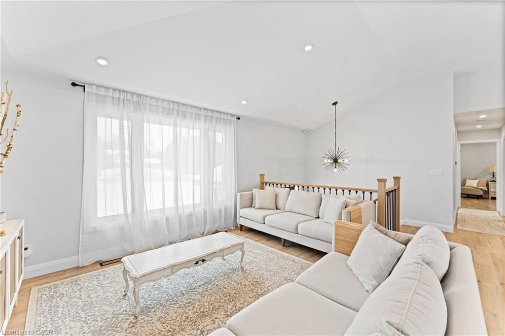 Furnished living room with white sofas, sheer-curtained window, patterned rug, and starburst pendant light.