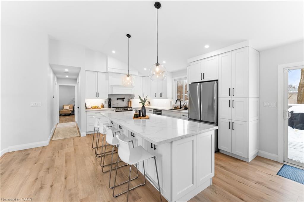 White kitchen with a large island, bar stools, stainless steel appliances, and snow visible outside.